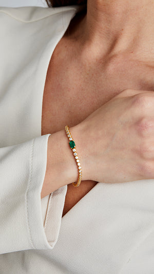 Gold slider bracelet with round brilliant-cut stones and emerald-green center stone.